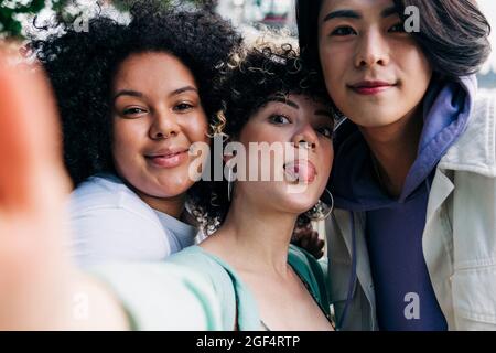 Junge Frau, die beim Selfie mit multiethnischen Freunden aus der Zunge ragt Stockfoto