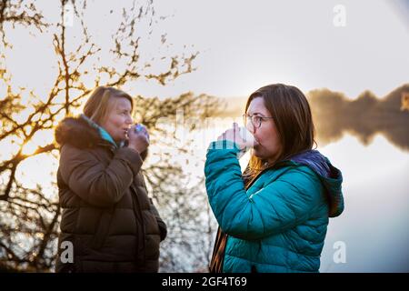 Weibliche Freunde trinken Kaffee am Morgen am Wasser Stockfoto