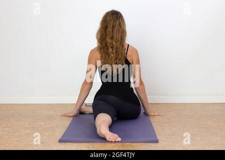 Rückseite der weiblichen Yogi in Schwanenpose auf Matte über weißem Hintergrund. Schlanke Frau auf schwarzen Overalls tun eka pada rajakapotasana drinnen, Hüften öffnen Stockfoto