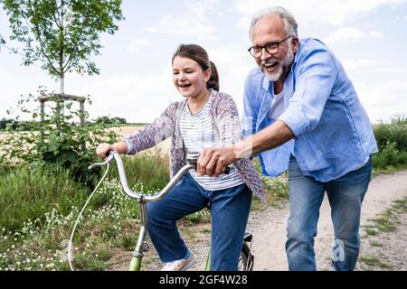 Fröhlicher Großvater spielt mit Enkelin, die auf unbefestigten Straßen unterwegs ist Stockfoto