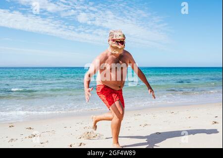 Mann mit Eidechsmaske, der mit gekreuzten Armen am Strand steht Stockfoto