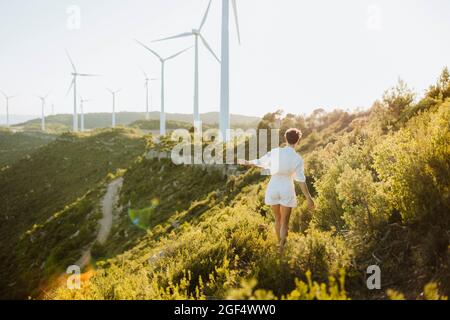 Frau, die während des Sonnenuntergangs in Richtung Windturbinen auf dem Berg geht Stockfoto