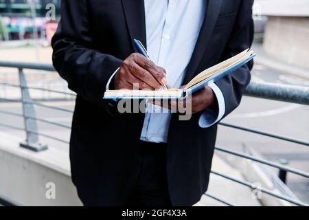 Ein Geschäftsmann, der sich auf das Geländer stützt und Tagebuch schreibt Stockfoto