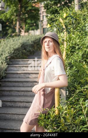 Porträt einer schönen jungen kaukasischen Frau in weißem T-Shirt, Himbeer-Sundress und Hut im Park stehen. Lange blonde Haare. Hochwertige Fotos Stockfoto