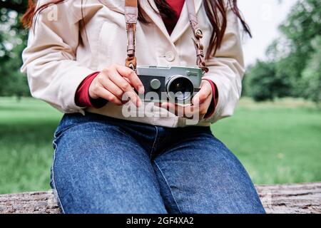 Frau mit alter Analogkamera, während sie auf einem umgestürzten Baum sitzt Stockfoto