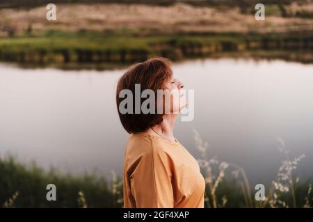 Ältere Frau mit geschlossenen Augen am Seeufer Stockfoto