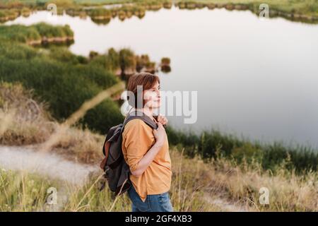 Ältere Frau mit Rucksack, die am Seeufer auf dem Trail steht Stockfoto