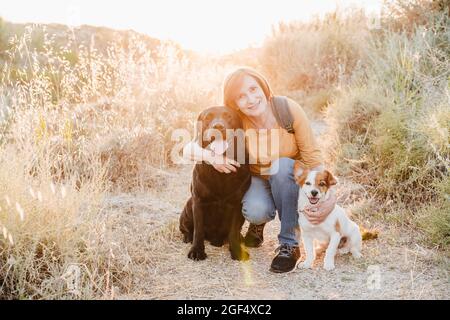 Frau umarmt Hunde, während sie auf der Spur hocken Stockfoto