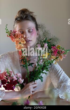 Schöne Frau mit erröten Gesicht hält Wildblumen im Studio Stockfoto