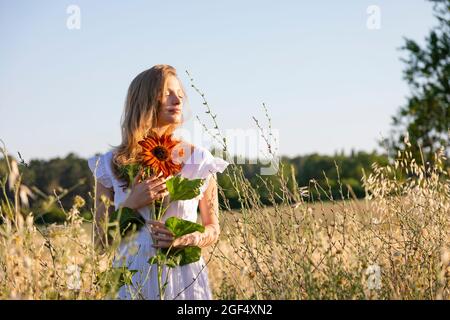 Schöne junge Frau mit geschlossenen Augen und Sonnenblume auf dem Feld Stockfoto