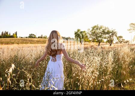 Blonde junge Frau in weißem Kleid, die mitten im Gras auf dem Feld läuft Stockfoto