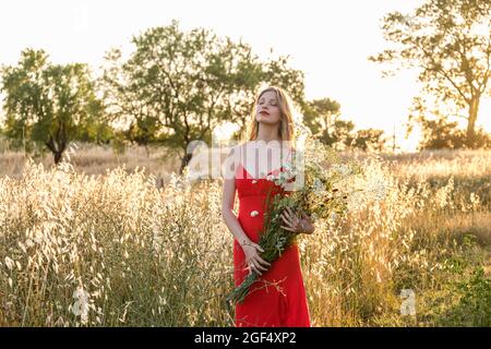 Junge schöne Frau mit geschlossenen Augen hält Wildblumen Bouquet im Feld Stockfoto