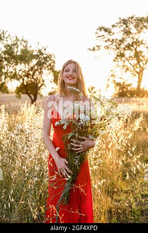 Lächelnde junge Frau mit Blumenstrauß auf dem Feld Stockfoto