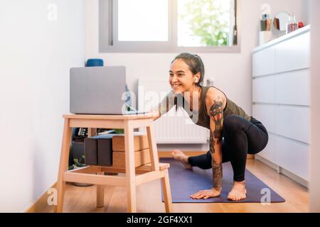 Lächelnde Frau, die zu Hause online über einen Laptop Yoga praktiziert Stockfoto