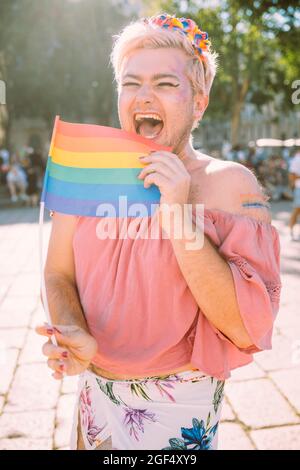 Fröhlicher schwuler Mann, der am sonnigen Tag mit Regenbogenfahne lacht Stockfoto