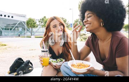 Glückliche multiethnische Freundinnen, die beim Essen reden Stockfoto