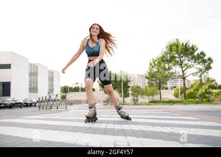 Lächelnde junge Rothaarige Frau, die in der Stadt auf der Straße Schlittschuh laufen Stockfoto