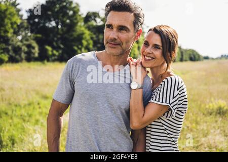 Lächelnde Frau, die sich auf der Wiese auf die Schulter des Mannes lehnt Stockfoto