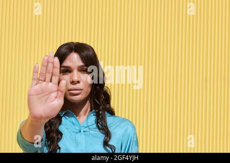 Nicht-binäre Frau mit Stop-Geste vor der gelben Wand Stockfoto