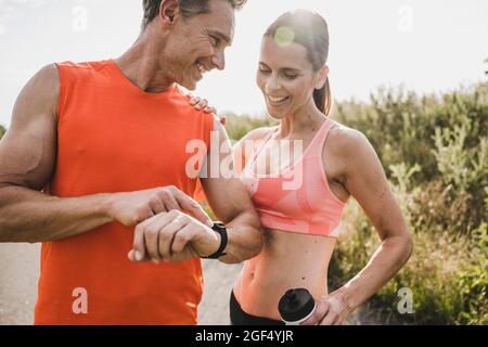 Lächelnder Sportler zeigt der Frau die Armbanduhr Stockfoto