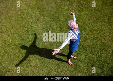 Reife Frau mit ausgestreckten Armen auf Gras an sonnigen Tagen Stockfoto