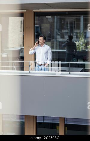 Geschäftsmann, der auf dem Bürobalkon steht und mit dem Mobiltelefon telefoniert Stockfoto