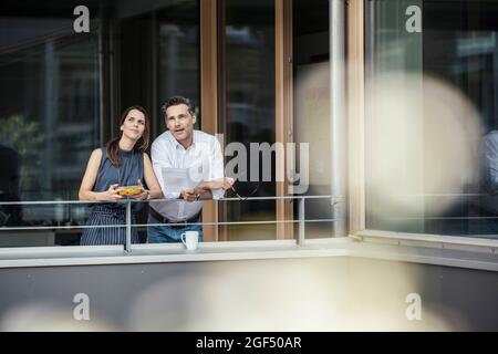 Männliche und weibliche Profis, die beim Anlehnen auf Geländer nachsinnen Stockfoto