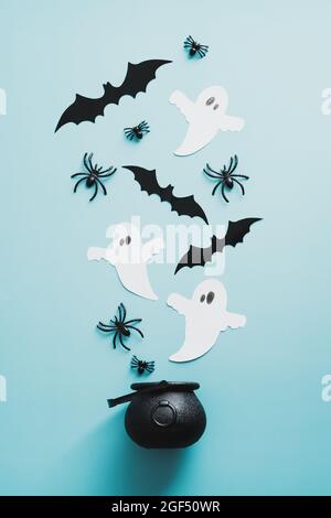 Gruselige böse Geister und Hexentopf auf blauem Hintergrund. Flach liegend, Draufsicht Spinnen, Papier Geister, Fledermäuse. Stockfoto