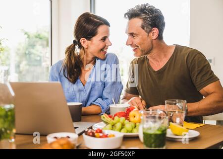 Lächelndes Paar, das sich beim Frühstück zu Hause ansieht Stockfoto