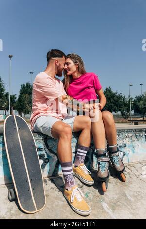 Junges Paar, das am sonnigen Tag im Skateboard Park von Angesicht zu Angesicht sitzt Stockfoto
