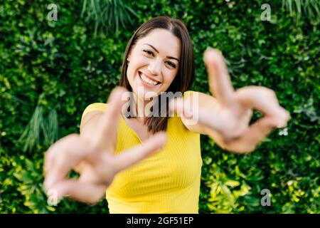 Glückliche junge Frau gestikuliert Friedenszeichen Stockfoto