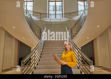 Lächelnde Geschäftsfrau, die das digitale Tablet hält, während sie vor der Treppe steht Stockfoto