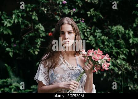 Junge Frau mit Blumenstrauß vor Efeupflanzen Stockfoto