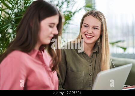 Glückliche weibliche Praktikantin im Teenageralter, die eine Geschäftsfrau mit einem Laptop ansieht, während sie während des Trainings im Büro diskutiert Stockfoto