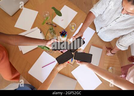 Im Büro halten Männer und Frauen Smartphones über dem Schreibtisch Stockfoto