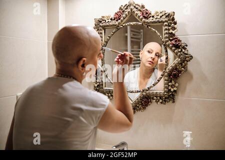 Reife Frau mit Krebs Bürsten Augenbraue, während Blick auf Reflexion im Spiegel Stockfoto