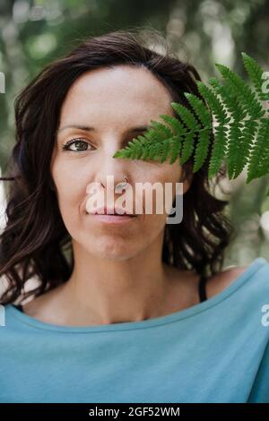 Frau, die im Wald das Auge mit Farnblättern bedeckt Stockfoto