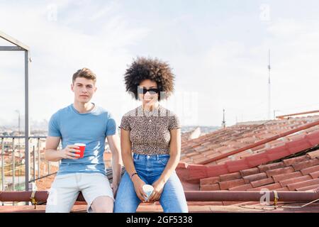 Männliche und weibliche Freunde mit Trinkbechern sitzen zusammen auf der Terrasse Stockfoto