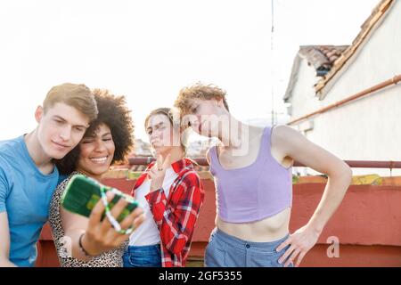 Lächelnde junge Freundinnen und Freundinnen, die gemeinsam Selfie auf dem Dach machen Stockfoto