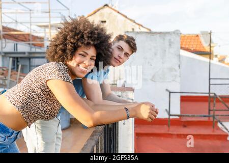 Lächelndes junges Paar, das sich auf der Terrasse am Geländer lehnt Stockfoto