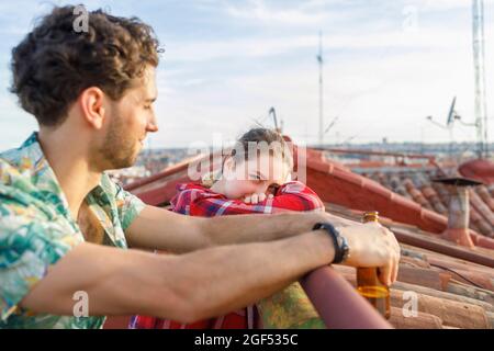 Junge Frau, die sich auf dem Dach von ihrem Freund auf das Geländer stützt Stockfoto