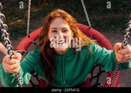 Glückliche junge Rotschopf Frau genießen auf Schaukel auf Spielplatz Stockfoto