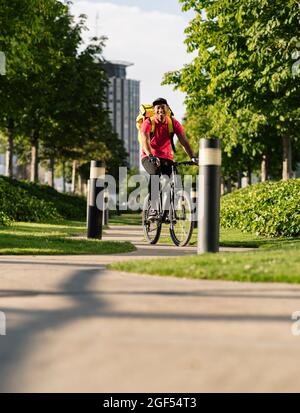 Lächelnder Lieferer, der an sonnigen Tagen im Park Fahrrad fährt Stockfoto