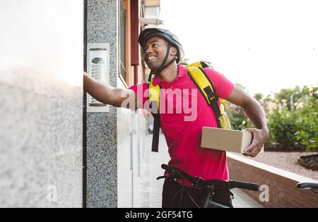 Lächelnder männlicher Lieferer hält das Paket, während er die Türklingel klingelt Stockfoto