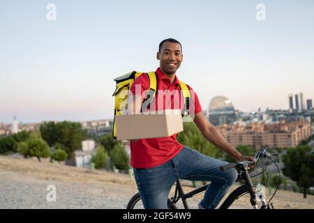 Lächelnder Lieferer gab Paket, während er auf dem Fahrrad saß Stockfoto