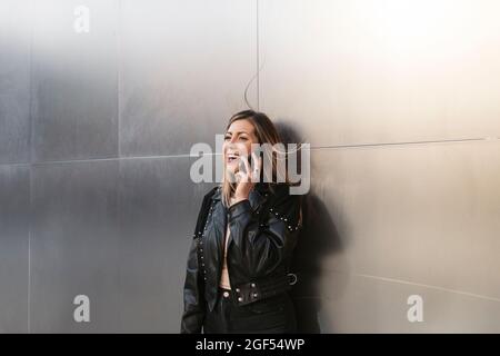 Junge Frau, die vor einer silbernen Wand mit einem Smartphone spricht Stockfoto