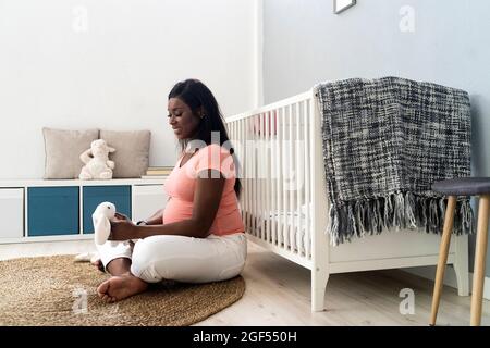 Glückliche Schwangere, die zu Hause auf dem Teppich sitzend ein Stofftier ansieht Stockfoto