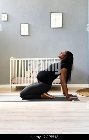 Junge Schwangere lehnt sich zurück, während sie im Schlafzimmer Yoga praktiziert Stockfoto