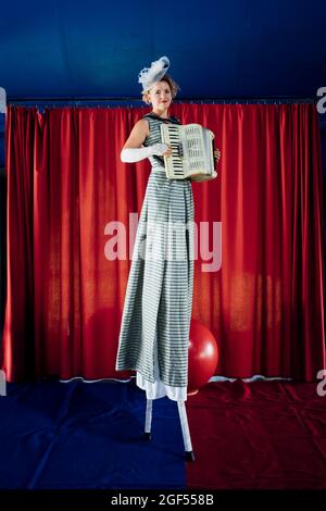 Eine Künstlerin spielt Akkordeon, während sie mit Stelzen auf der Bühne läuft Stockfoto