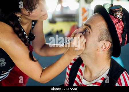 Weibliche Make-up-Künstlerin, die hinter der Bühne Eyeliner auf männliche Künstler anwendet Stockfoto